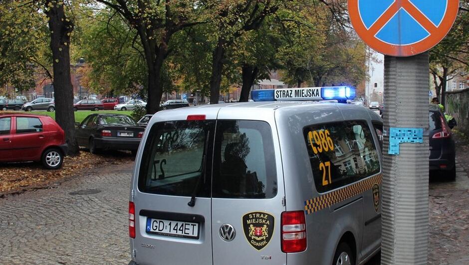 radiowóz zaparkowane samochody wybrukowana ulica plac Wałowy drzewa trawnik znak drogowy zakaz zatrzymywania strażnicy