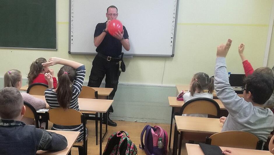 strażnik z czerownym balonem klasa uczniowie tornistry ławki tablice na ścianie