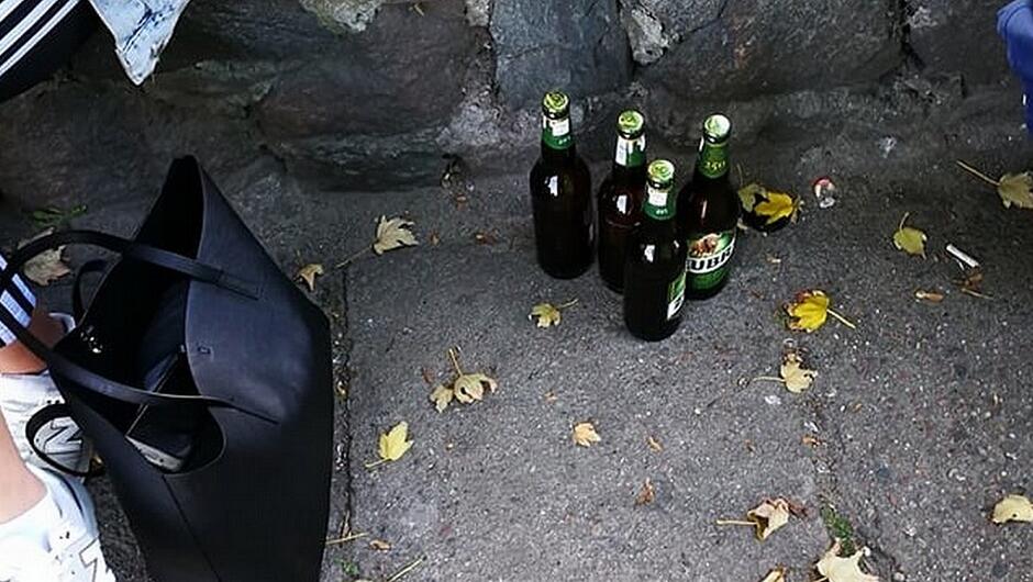 cztery butelki piwa murek z kamieni fragment siedzącej osoby damska torba żółte liście