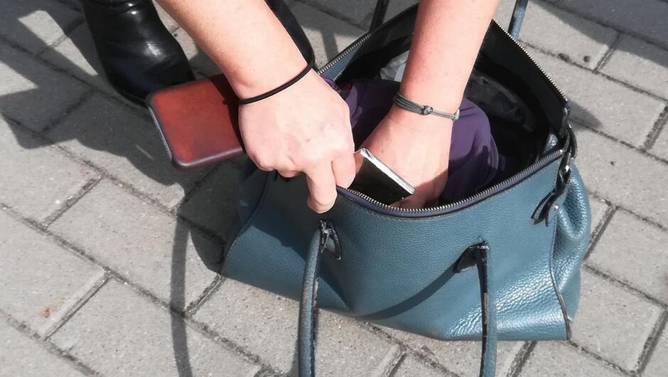 Damska torebka telefon komórkowy fragment chodnika wyłożony kostką brukową damskie dłonie włożone do torebki