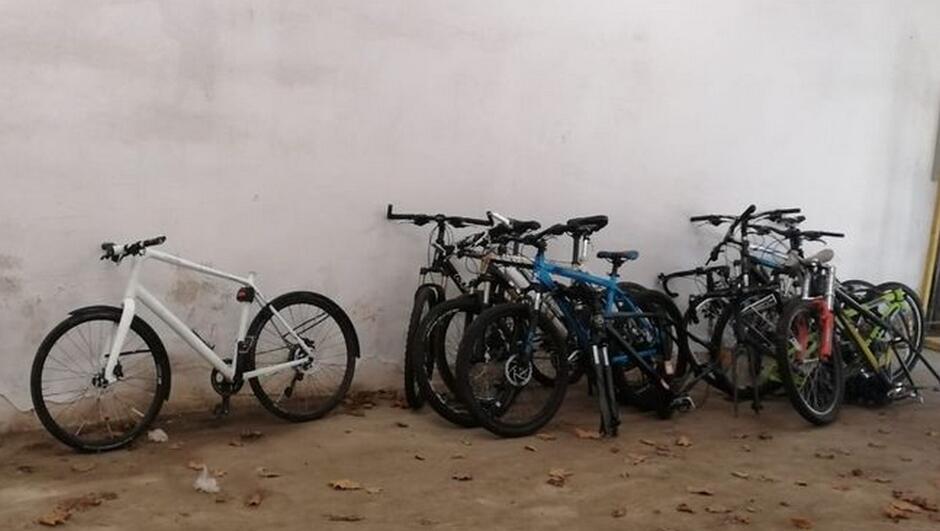 rowery stoją na ziemi, oparte o białą ścianę,