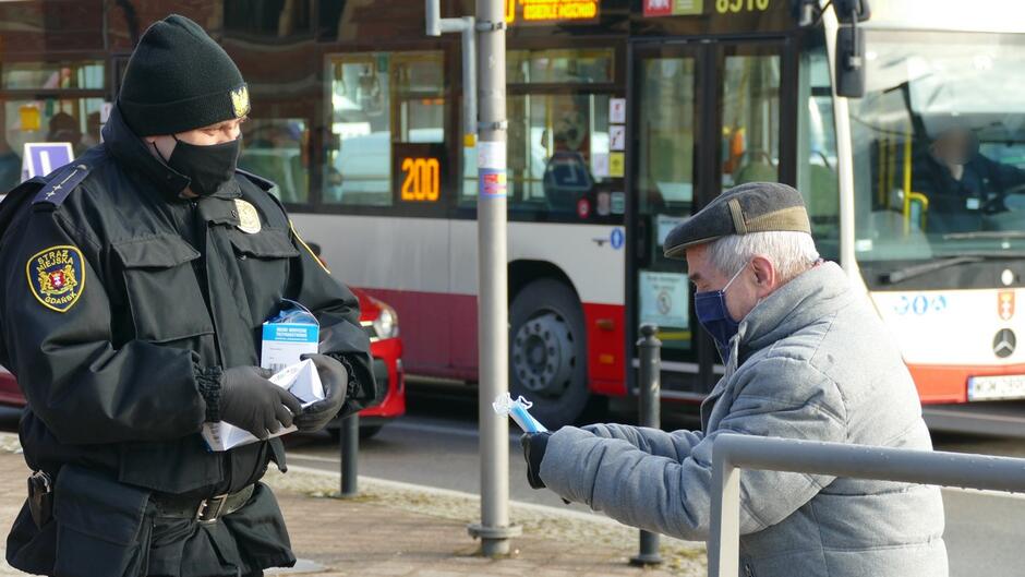 strażnik wręcza maseczki starszemu mężczyznie autobus linii 200.JPG